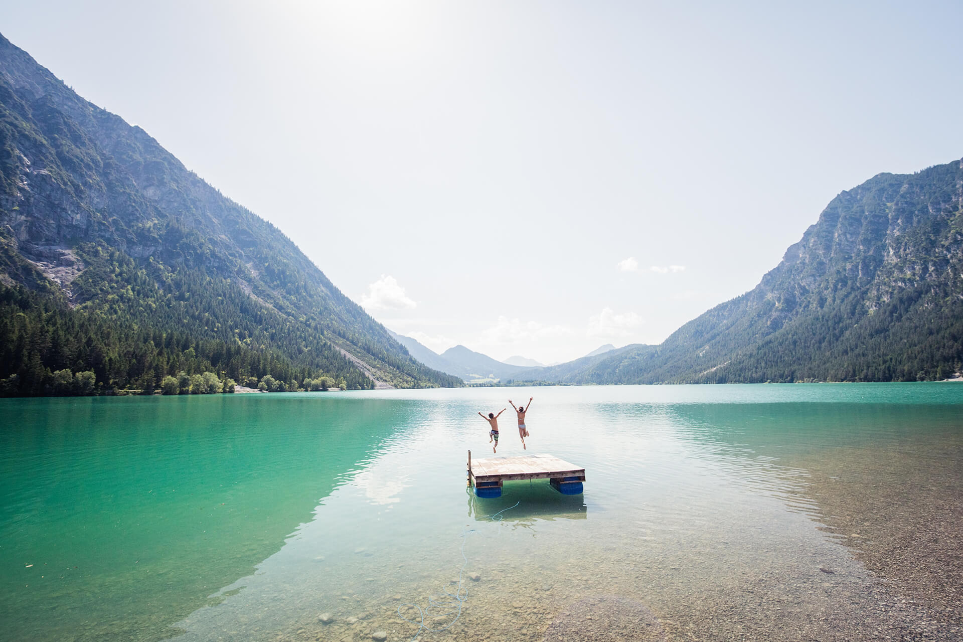 Zwei Kinder springen auf einer schwimmenden Plattform mitten im See in die Luft